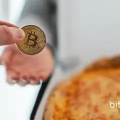 Dłoń trzyma monetę z symbolem Bitcoina, obok pizzy. Zastanawiasz się, ile kosztował bitcoin 10 lat temu?