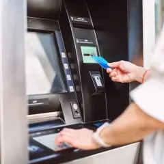 Kobieta wkłada kartę do bankomatu, przygotowując się, jak wziąć debet. Wpisuje PIN na klawiaturze.
