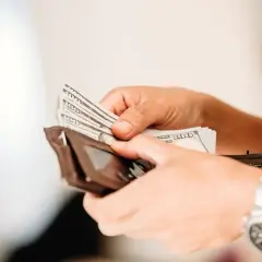 Ręce liczą banknoty 100 dolarowe, przygotowując się do wypłaty pieniędzy z Revolut.