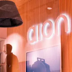 Jasne, oto propozycja:

Logo Aion Bank S.A. świeci na pomarańczowej ścianie. W tle widać cień postaci i regały.