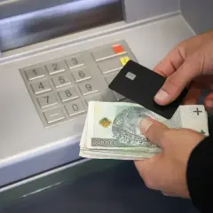 Ręce trzymające kartę i plik banknotów przy bankomacie. Dowiedz się, jak wpłacić pieniądze na konto.