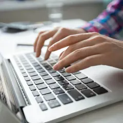 Dłonie piszą na laptopie. Szukasz informacji, gdzie zgłosić oszustwo sklepu internetowego?