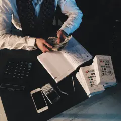 Mężczyzna liczy pieniądze, obok kalkulator, telefony i pudełka z iPhone'ami. Zastanawia się, ile powinna wynosić poduszka finansowa.