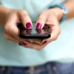 Dłonie z malowanymi paznokciami piszą na telefonie, szukając informacji, jak zmienić limit w IKO na telefonie.