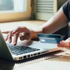 Osoba wpisuje dane na laptopie, trzymając kartę płatniczą. Dowiedz się, jak zablokować kartę ipko w razie potrzeby.
