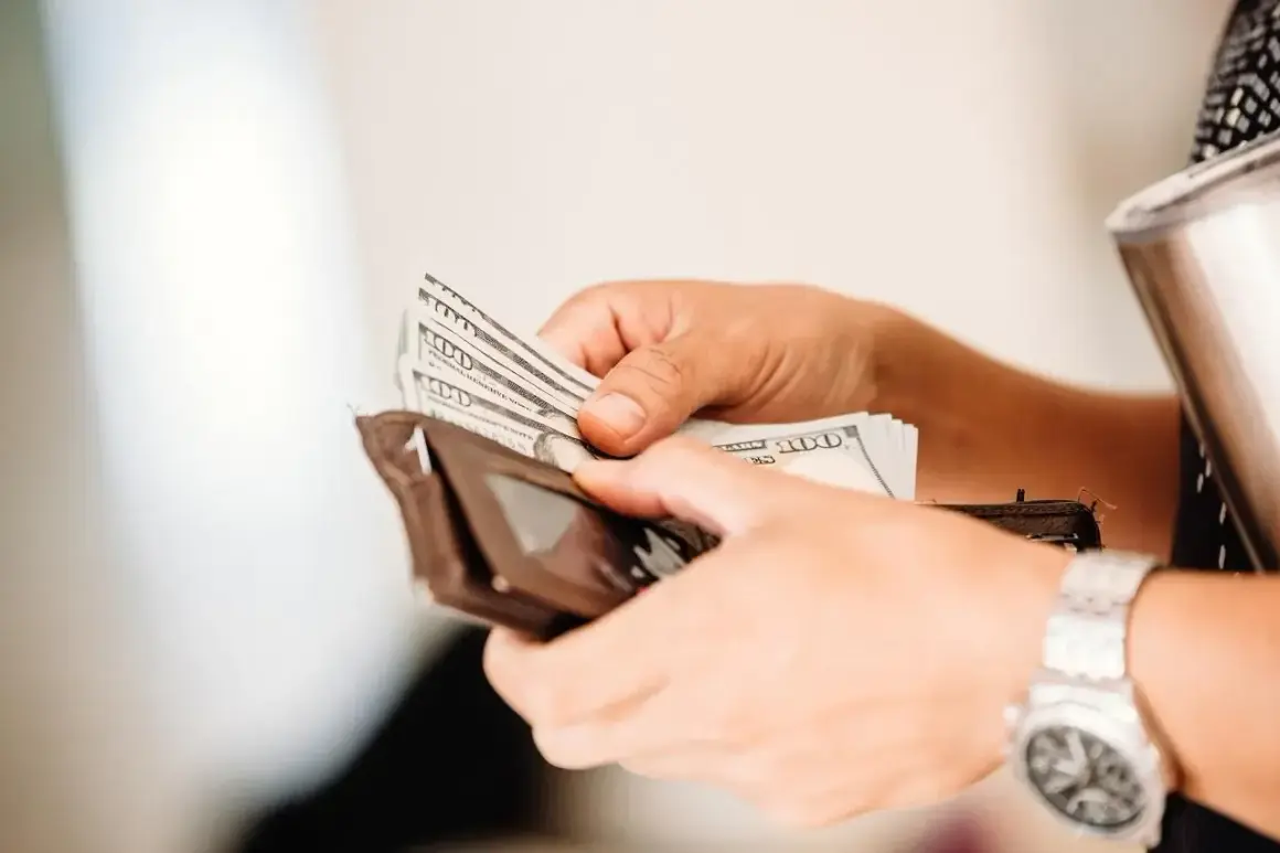 Ręce liczą banknoty 100 dolarowe, przygotowując się do wypłaty pieniędzy z Revolut.