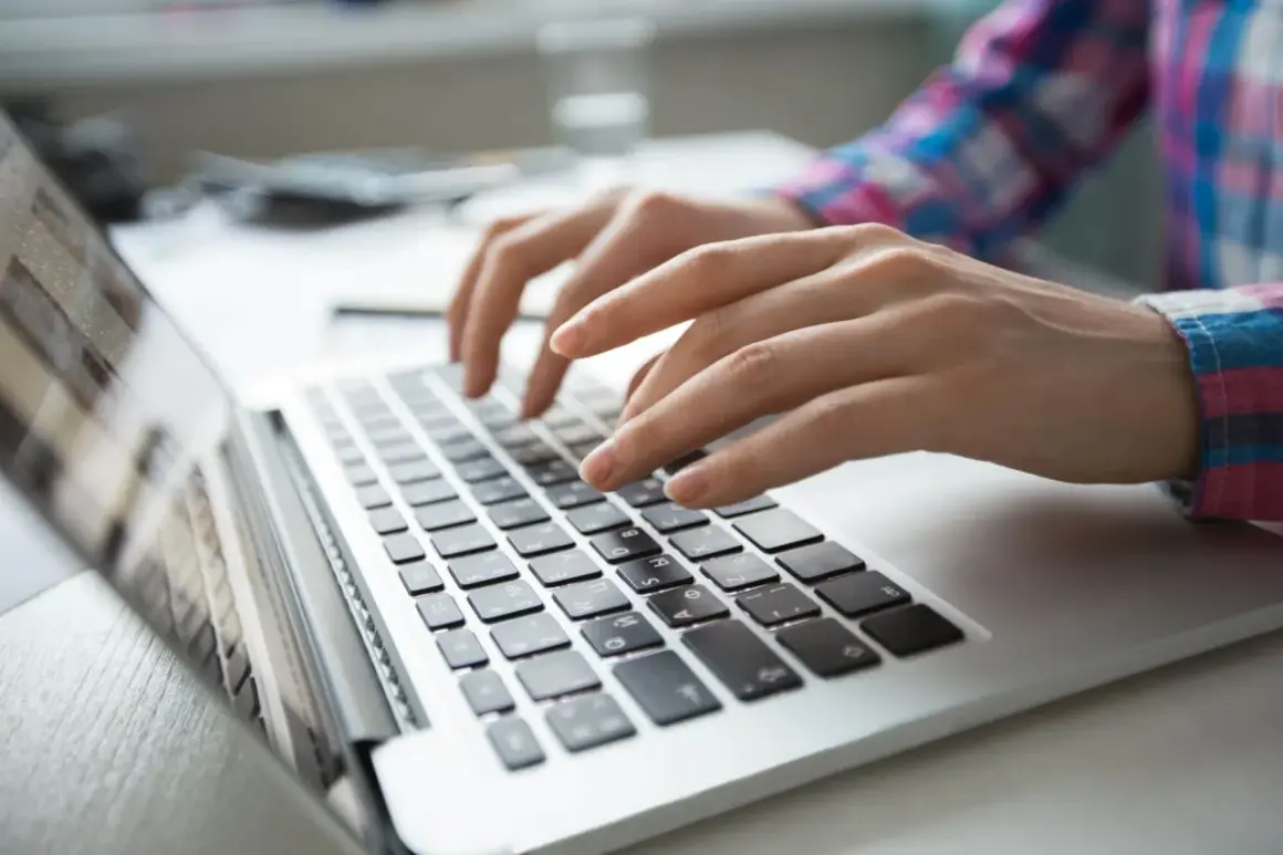 Dłonie piszą na laptopie. Szukasz informacji, gdzie zgłosić oszustwo sklepu internetowego?