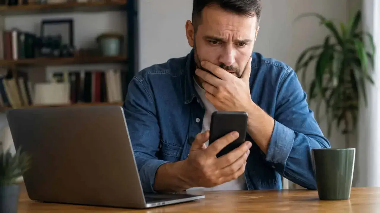 Zmartwiony mężczyzna szuka informacji, jak odzyskać pieniądze z przelewu oszustwa, trzymając telefon.