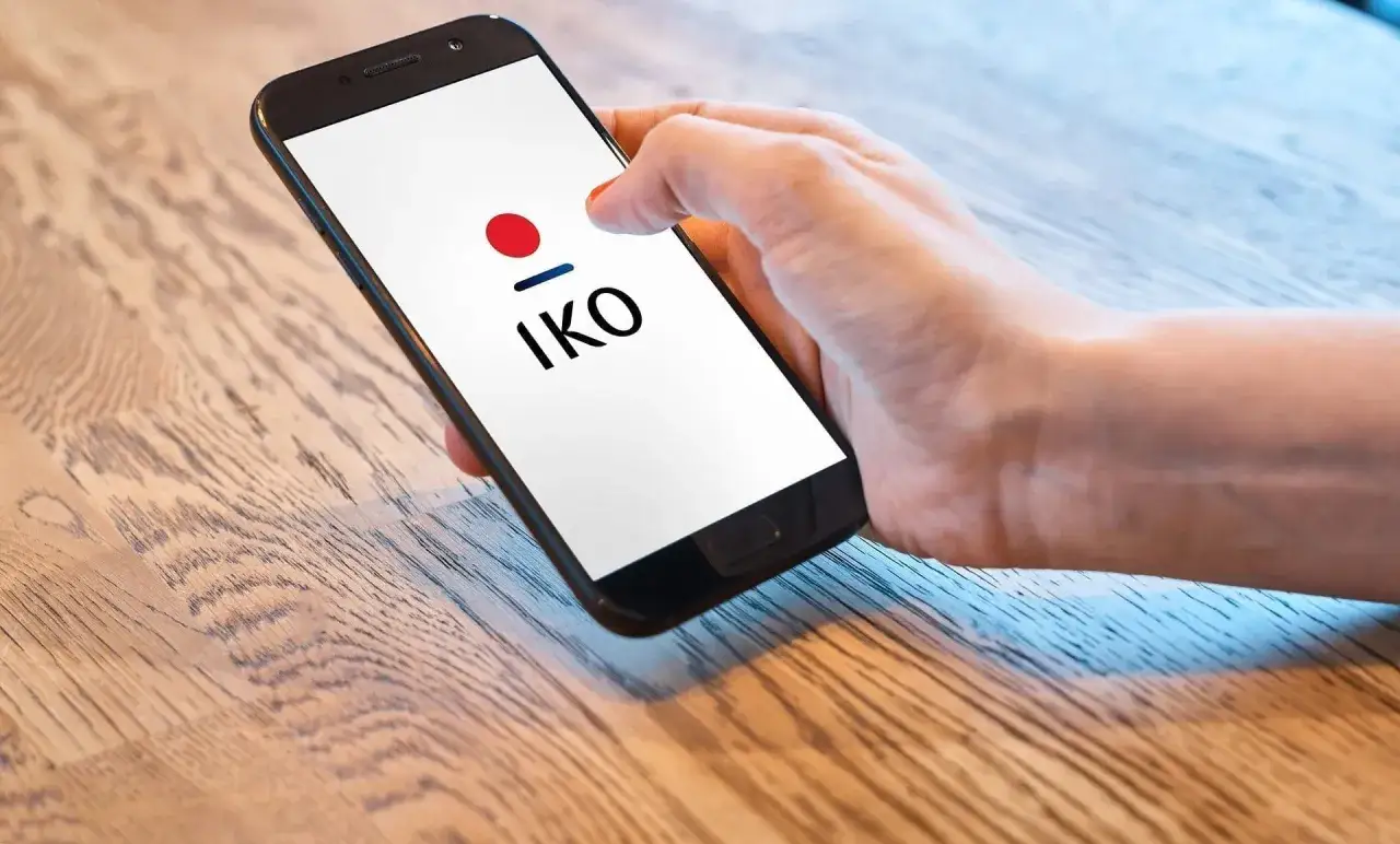 Dłoń trzyma smartfon z logo IKO. Dowiedz się, jak zmienić limit w IKO na telefonie, aby bezpiecznie zarządzać finansami.