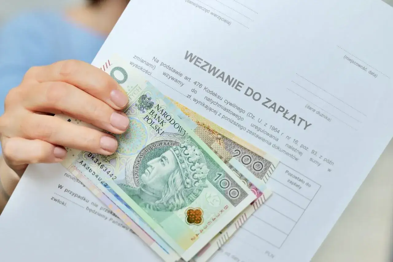Ręka trzyma wezwanie do zapłaty i polskie banknoty. To może być sposób na zabezpieczenie konta bezpiecznego od komornika.